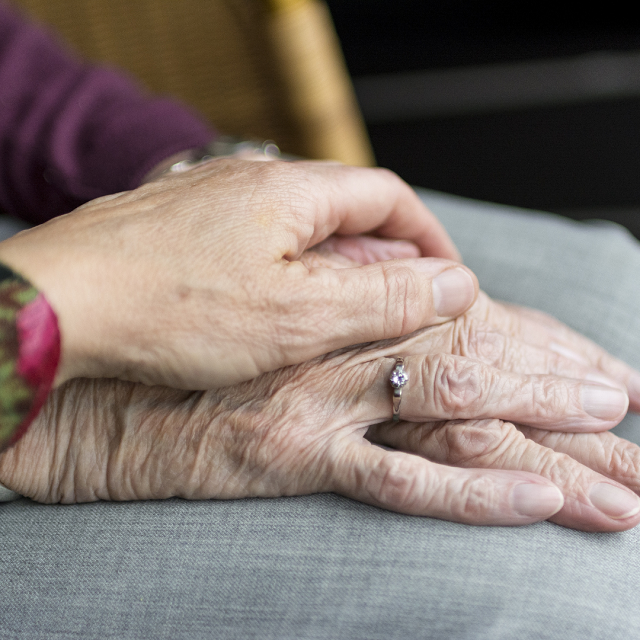Photo of a hand placed reassuringly over the top of an older person's hand.