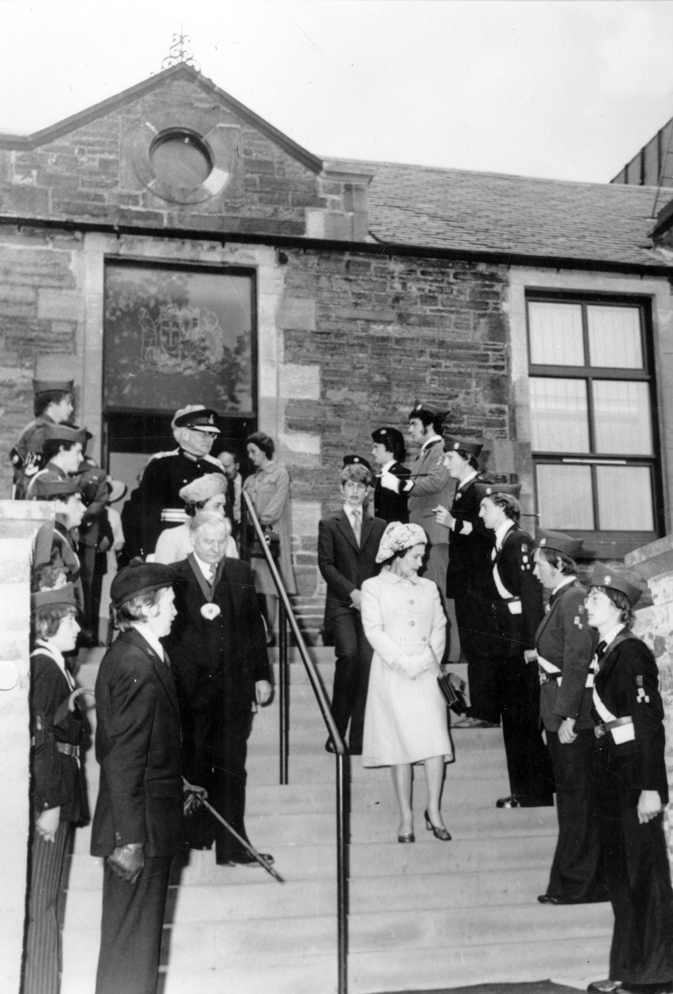 A black and white photo with men and women standing on steps with a railing between them
