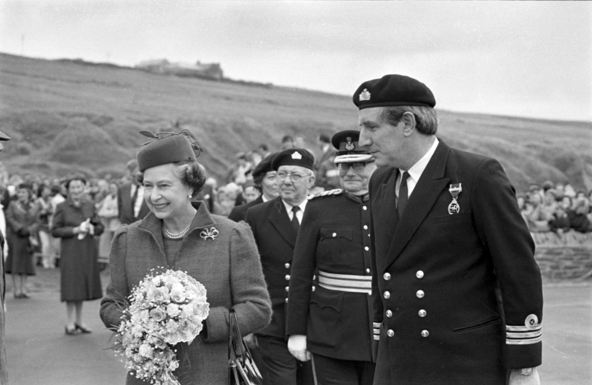 a black and white photo with the queen in 1987 with men in suits beside her all lined up