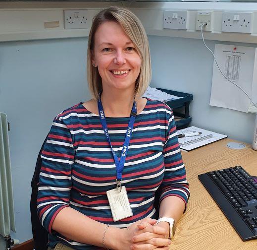 a lady smiling at her desk with a blue lanyard round her neck