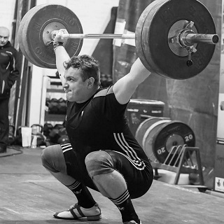 a man holding weights, squatting down and his face showing they are heavy
