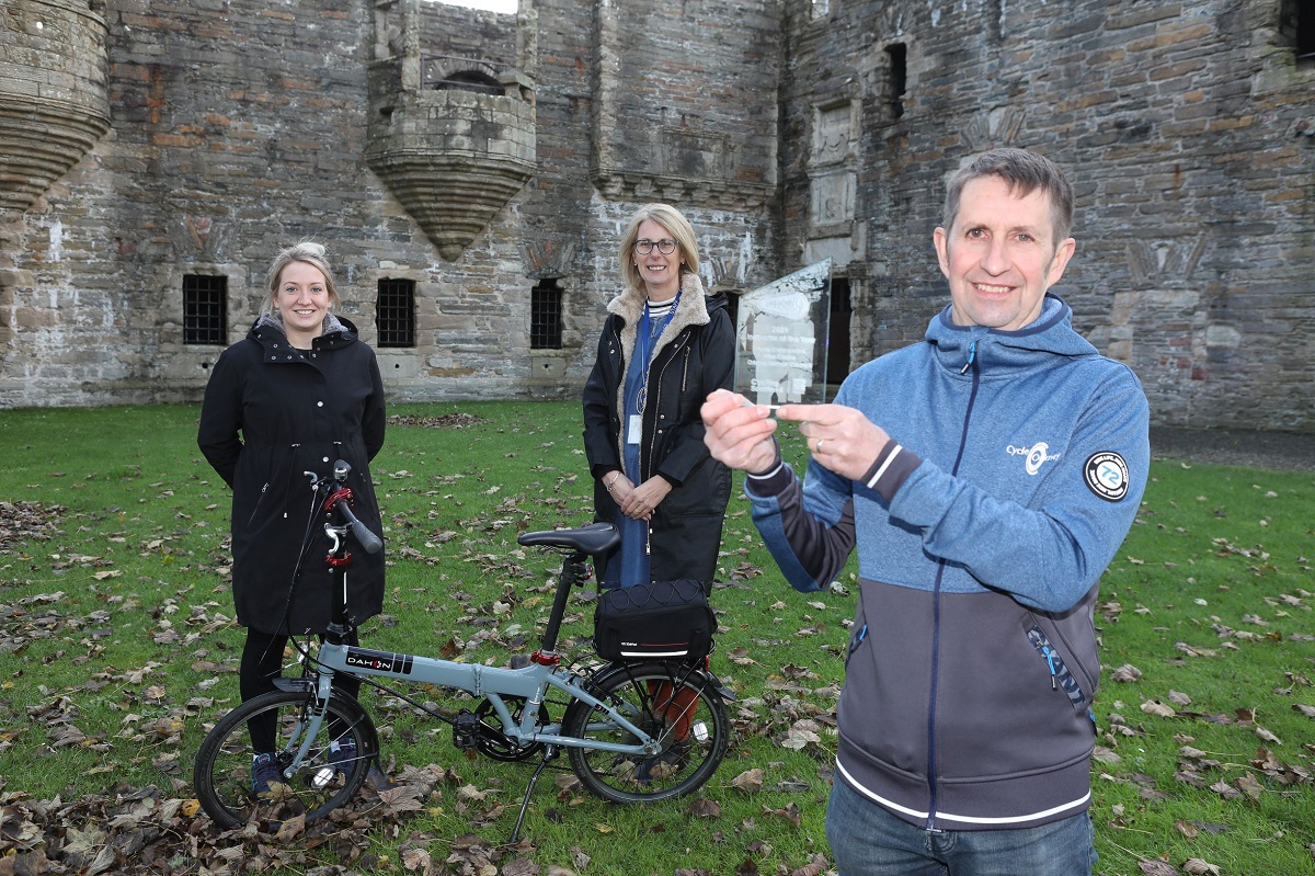 2 ladies and a man holding an award with a bike in the foreground