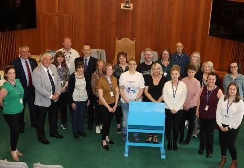 a group of people in a room surrounding a blue rotating 'raffle' machine'