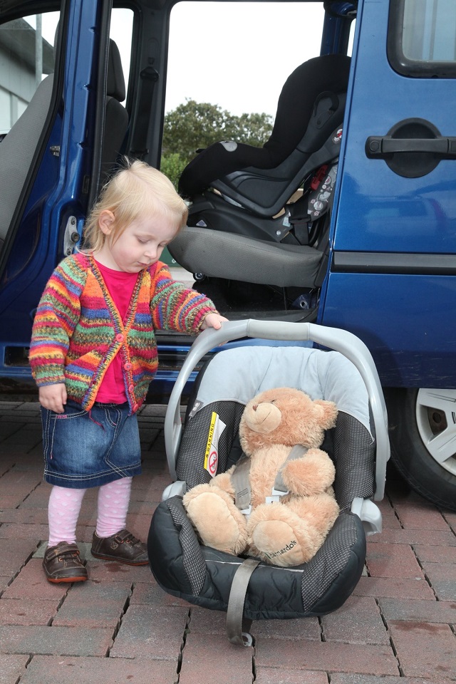 a small girl looking at her teddy in a car seat