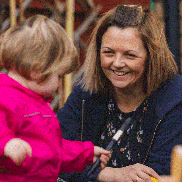 A photo of a lady smiling at a toddler