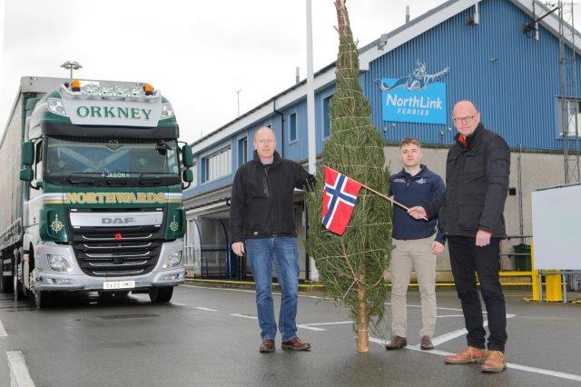 3 men standing in front of a Christmas tree holding a Norwegian flag