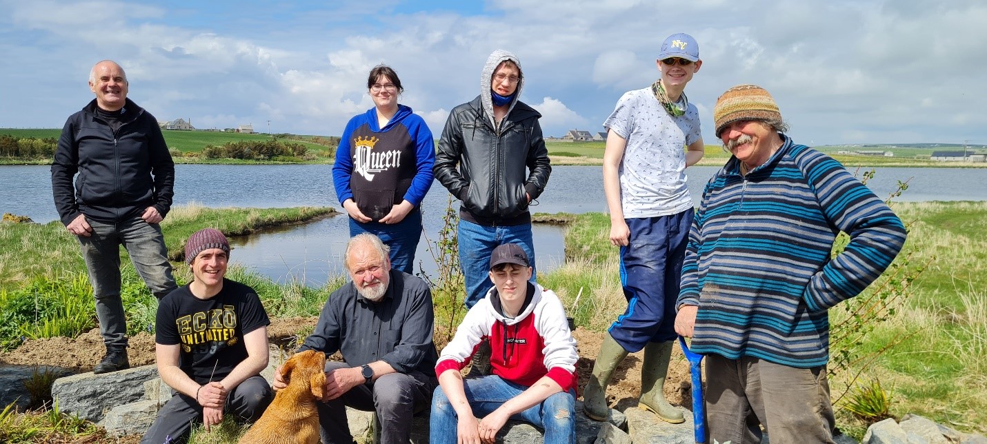 8 people standing and sitting at a loch with a dog