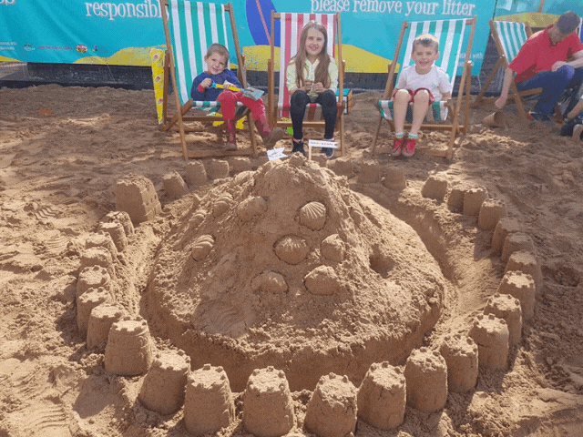 3 children sitting round a huge sandcastle with mini sandcastles around it