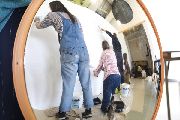 3 people painting a white wall with a circular mirror facing them
