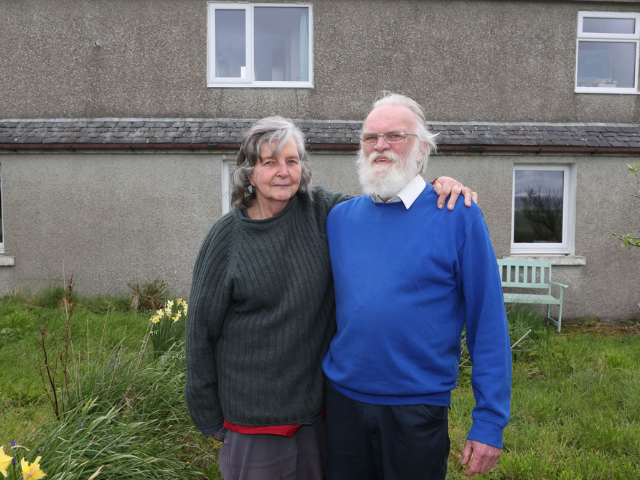 a man and a lady standing with their arms around each other in front of a house