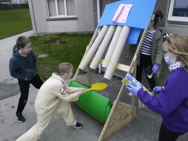 3 children playing a home made game with cardboard tubes