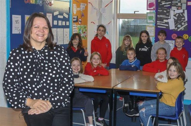 a lady sitting in front of a class of children gathered round a table