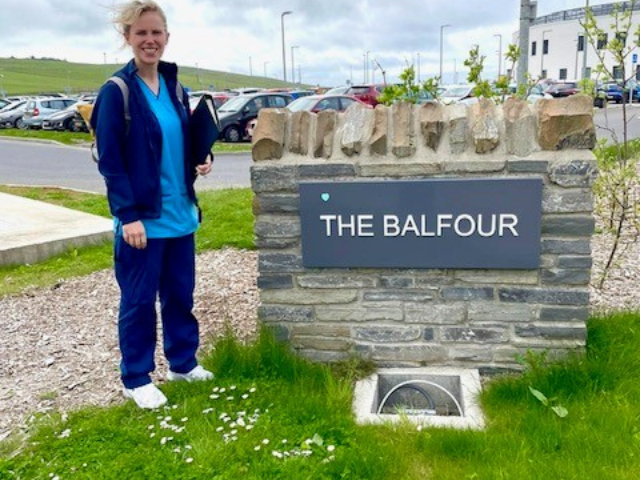 a lady standing next to the Balfour Hospital sign