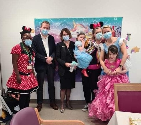 5 adults and 2 children, the children are dressed up as disney princesses all are wearing facemasks