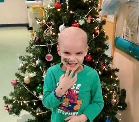 A young boy in hospital standing next to a Christmas tree