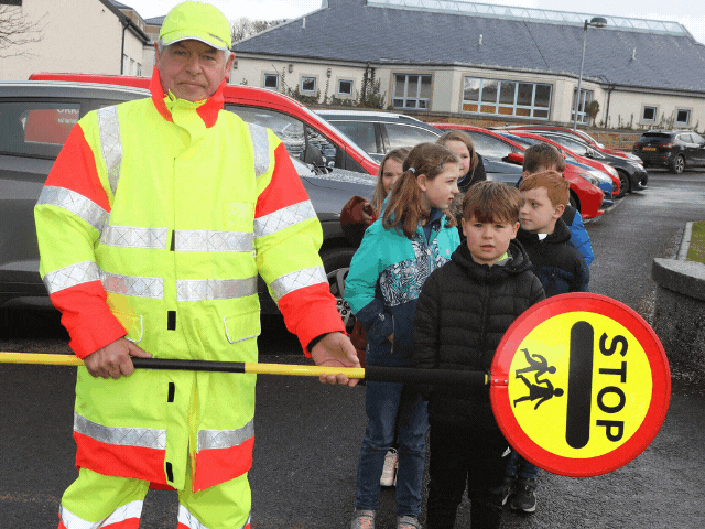 a lollipop man waiting to cross a road with children