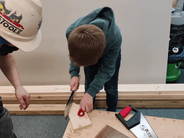 a young boy sawing with an adult watching