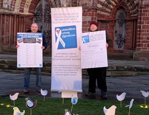 2 people standing outside St Magnus Cathedral holding posters