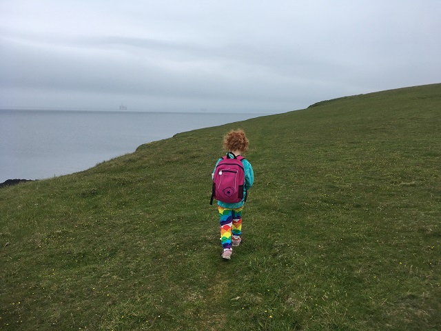 a little girl with a pink backpack out on a coastal walk