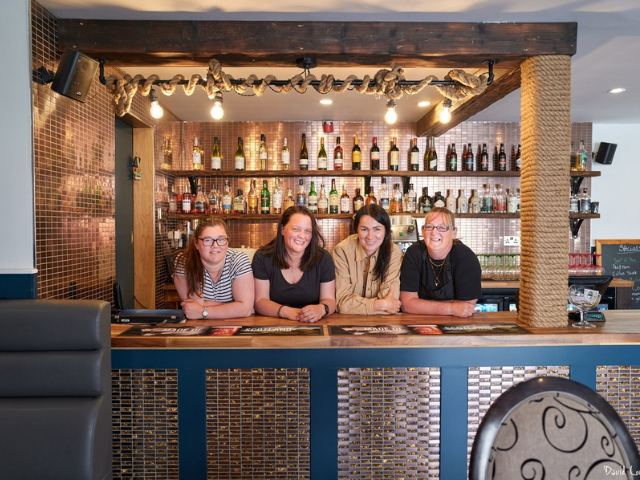 4 women standing behind a bar