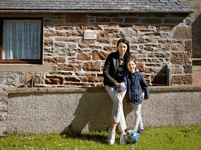 a lady and a child smiling in front of a house leaning against a wall