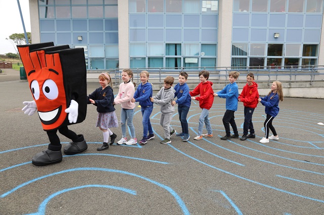 a foam red hand puppet with a huge smile doing a conga with 9 children behind it