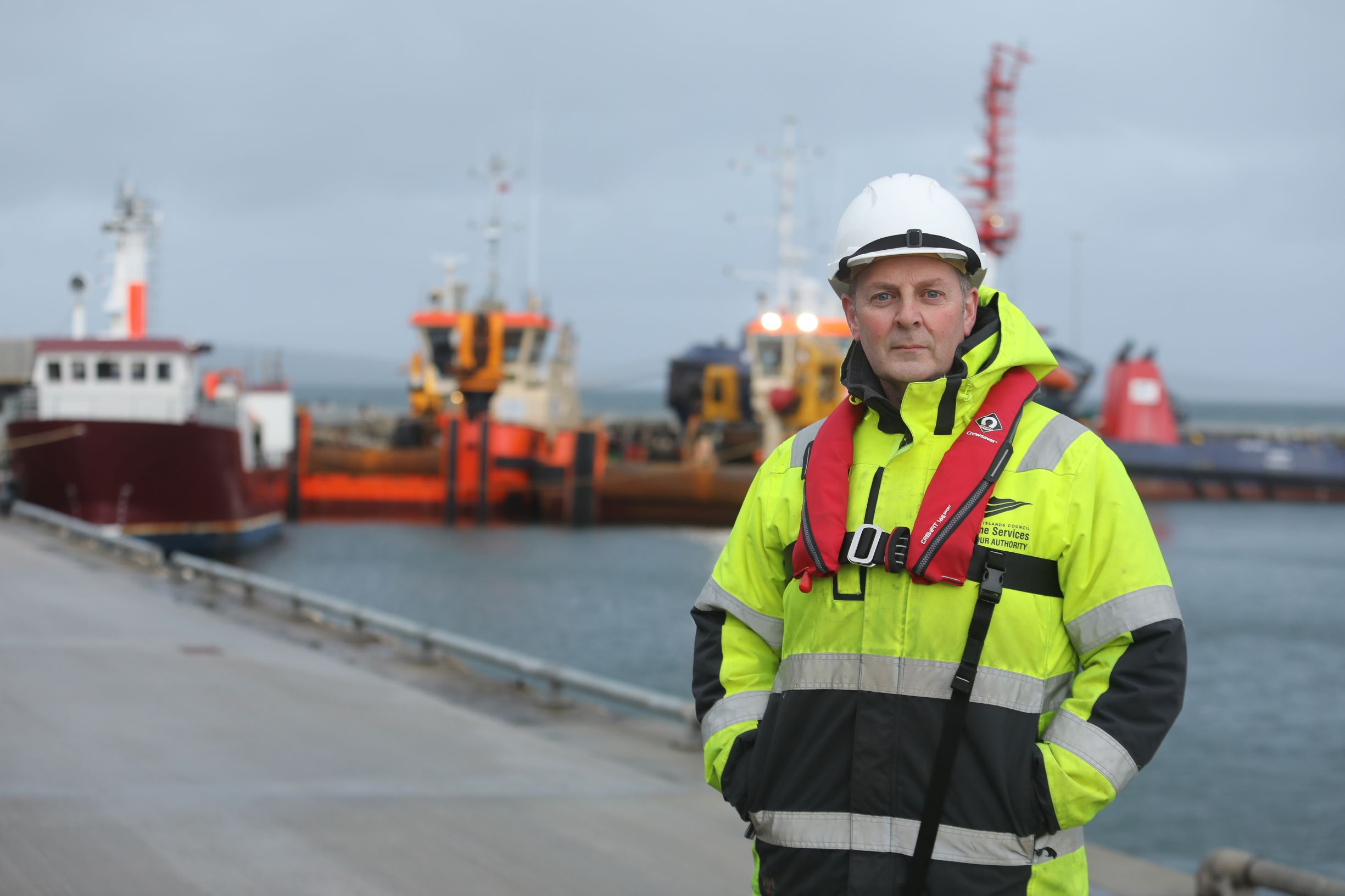 a man standing in a hi vis and a lifejacket and hard hat by the marina
