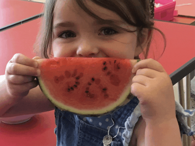 a small girl holding a watermelon up to her mouth - making it look like she is smiling