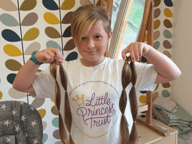 a little girl wearing a t-shirt saying little princess trust holding her cut hair