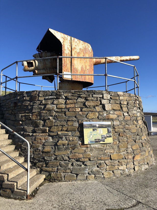 a stone wall with railings at top with an original Scapa flow gun at the top