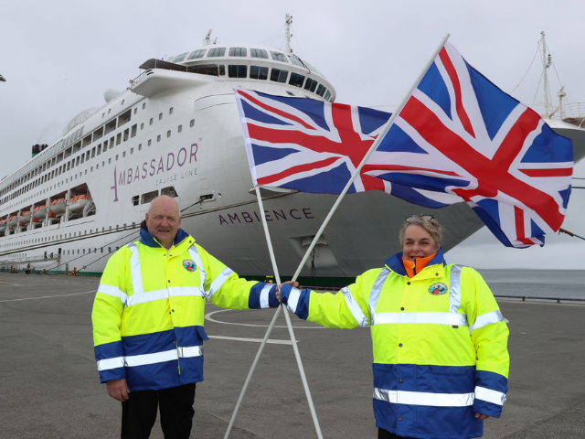 2 people holding 2 British flags with a cruise liner in the background