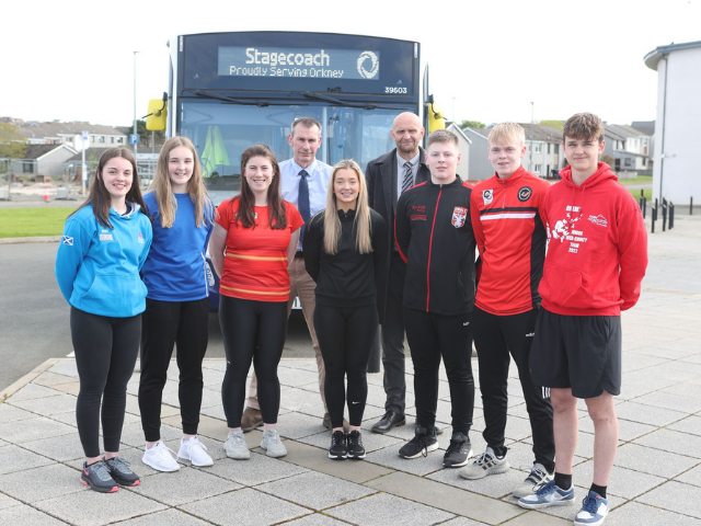4 girls, 3 boys in front of a bus with 2 adults behind