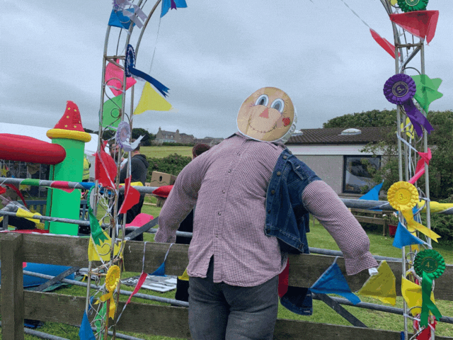 a stuffed scarecrow with a bannered arch in background