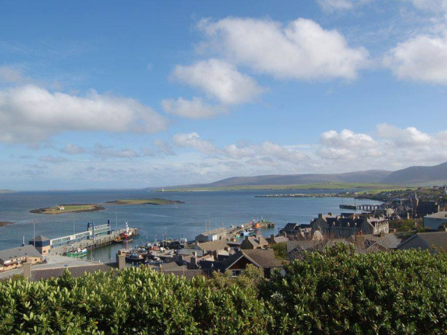 a landscape picture with the sea in the background, a pier and trees in the foreground