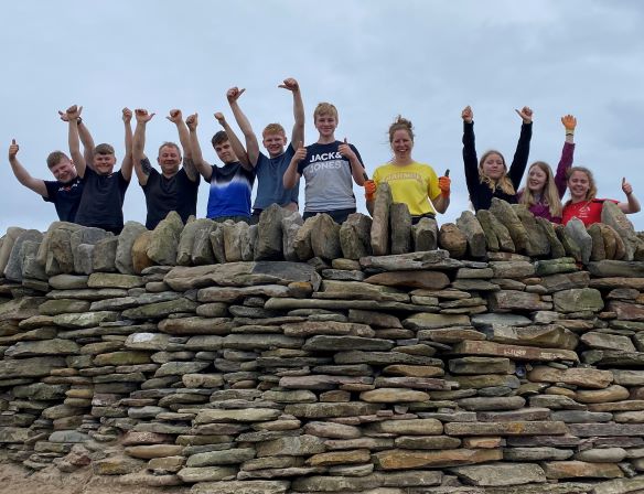 a group of children standing behind a stone wall with their hands up in the air