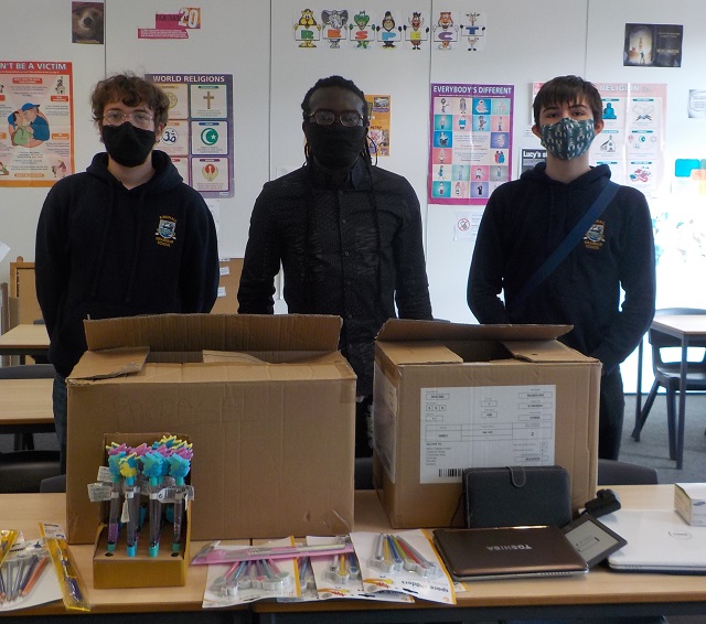 3 people standing in a classroom with 2 cardboard boxes in front of them