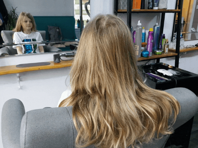 a small boy sitting in front of a mirror at hairdressers