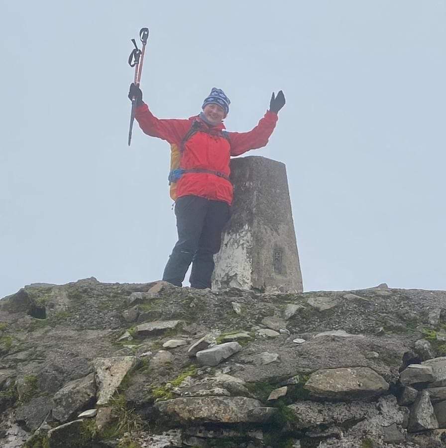 a lady with her hands in the air at the top of a mountain