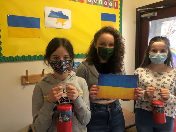 3 children wearing face masks holding a Ukraine flag